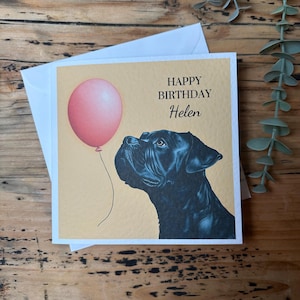 May include: A birthday card featuring a black dog looking up at a pink balloon. The card reads "Happy Birthday Helen".