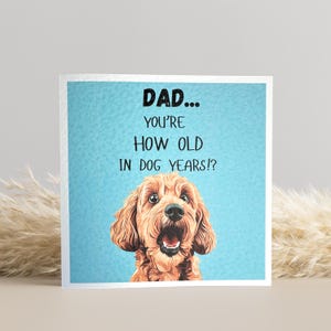 May include: A square greeting card with a light blue background and the text "DAD... YOU'RE HOW OLD IN DOG YEARS!?" A brown dog with an open mouth is featured below the text.