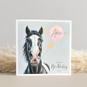 May include: A birthday card featuring a watercolour illustration of a black and white horse with a pink balloon that says "Adele" and the text "Happy Birthday to You".