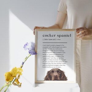 Könnte beinhalten: Ein gerahmter Druck mit der Definition eines Cocker Spaniels. Der Text beschreibt die Eigenschaften des Hundes, mit einer braunen Cocker Spaniel-Illustration unten. Der Rahmen ist hell.