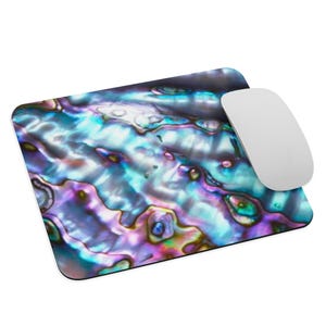 Puede incluir: Alfombrilla de ratón rectangular con un diseño iridiscente de concha de abulón en tonos azules, morados y verdes. Un ratón inalámbrico blanco descansa a la derecha, un accesorio de escritorio decorativo y funcional.