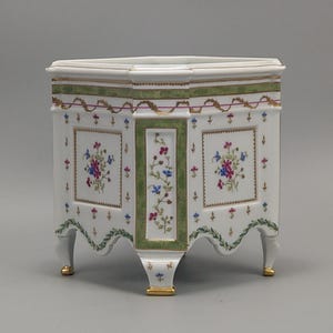 May include: White porcelain planter with a hexagonal top and three legs. The planter features floral designs in blue, pink, and red, framed by green and gold accents. The legs have gold detailing.