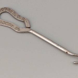May include: A silver shoe horn with a hook on the end. The handle is shaped like a loop and has the text "TO GRANT  ST. BUFFALO, N.Y." engraved on it.