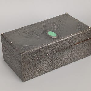Peut inclure: Boîte rectangulaire en métal avec une texture martelée et un motif floral sur le couvercle. La boîte présente un accent ovale vert et de petits clous dorés. Un objet de rangement décoratif.