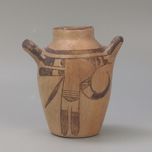 Puede incluir: Una pequeña olla de cerámica de color beige con dos asas. La olla está decorada con diseños pintados en negro de formas geométricas y una figura estilizada.