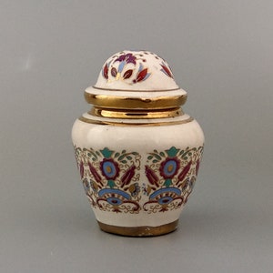 Può includere: Un piccolo vaso in ceramica bianca con un coperchio dorato e intricati disegni floreali in rosso, blu e verde.