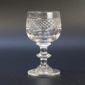 May include: A clear, stemmed glass with a diamond-cut pattern around the top. The glass has a round bowl, a slender stem with a bulbous detail, and a circular base. The glass is designed for serving beverages.