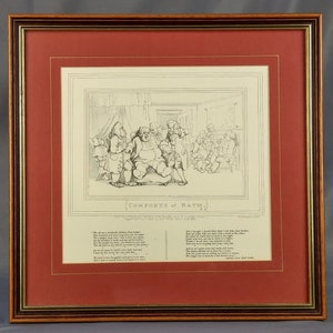 May include: A black and white engraving of a satirical cartoon titled "Comforts of Bath." The cartoon depicts a group of people in a room, with one man sitting on a chair and another man standing next to him. The engraving is framed in a red and gold frame.
