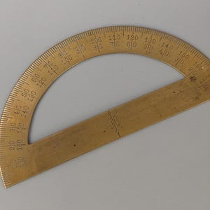 Peut inclure: Un rapporteur en laiton vintage avec des graduations de 0 à 180 degrés. L'outil a un bord droit et une échelle incurvée semi-circulaire. Les chiffres sont gravés dans le laiton. Le rapporteur est utilisé pour mesurer les angles.