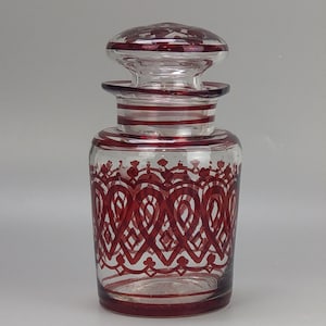 Puede incluir: Un frasco de vidrio transparente con un diseño estampado en rojo y blanco. El frasco tiene una tapa con un diseño similar.