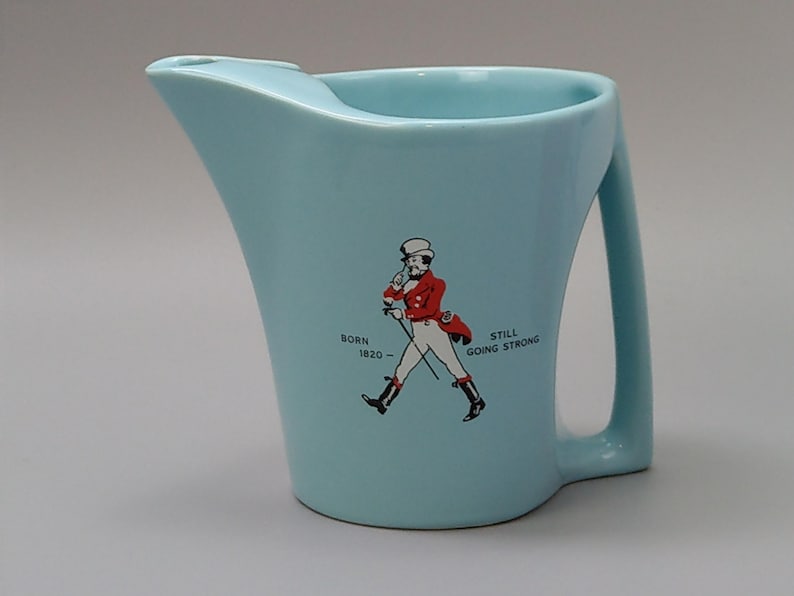 May include: Light blue ceramic pitcher with a handle and a pouring spout. The pitcher features a graphic of a man in a red coat and the text "Born 1820 - Still Going Strong."