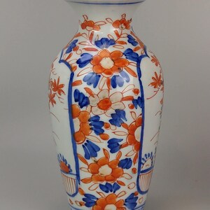 May include: A white porcelain vase with a blue and orange floral pattern. The vase has a narrow neck and a wide base. The floral pattern is intricate and detailed.