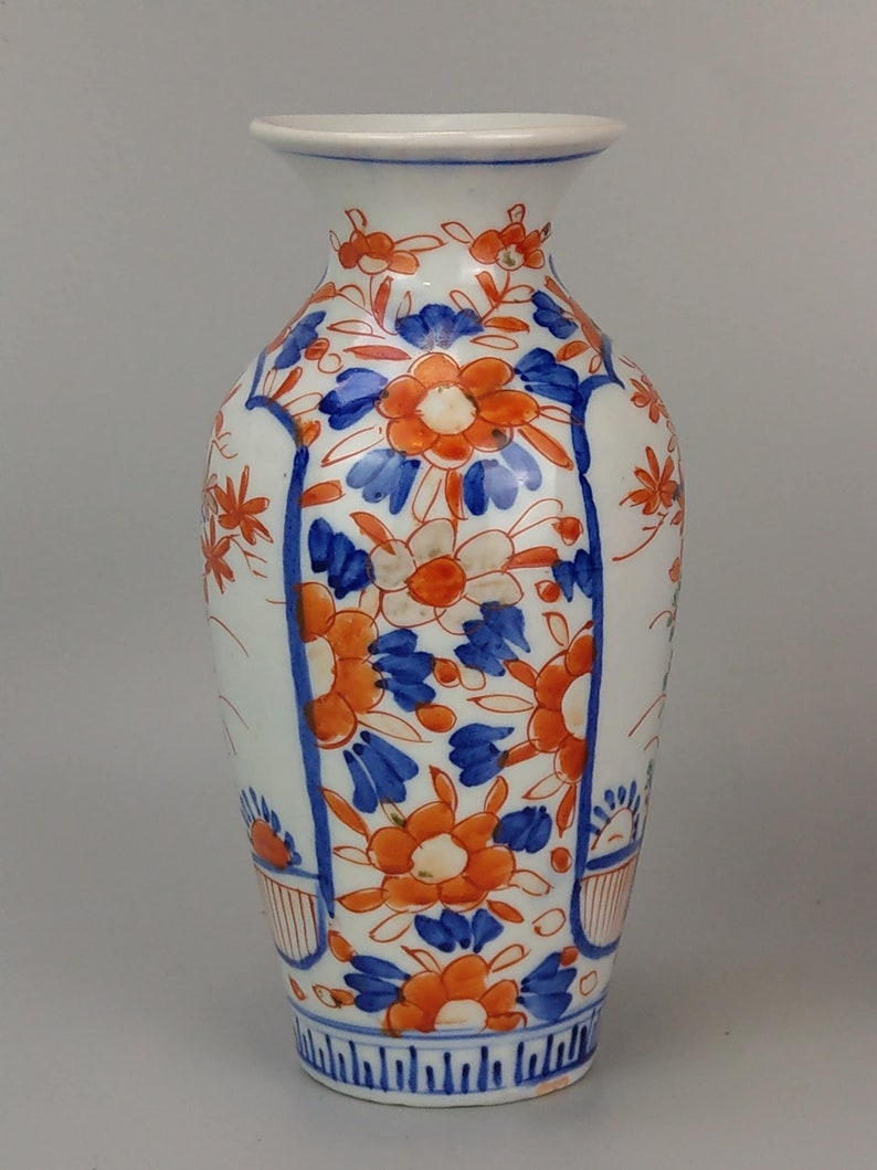 May include: A white porcelain vase with a blue and orange floral pattern. The vase has a narrow neck and a wide base. The floral pattern is intricate and detailed.
