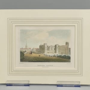 May include: An antique hand-colored engraving titled Newark Castle, Nottinghamshire, depicting a stone castle ruin with a church spire in the distance, set within a cream-colored mat board featuring decorative embossed lines and a rectangular border.
