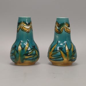 May include: Two turquoise ceramic vases with yellow and white wave patterns at the top and yellow and green leaf-like designs at the base. The vases have a bulbous shape and are displayed against a plain background.