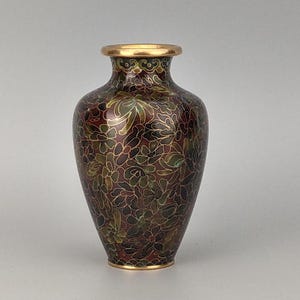 Pode incluir: Um pequeno vaso cloisonné com um fundo bordô profundo adornado com um padrão denso e intrincado de motivos florais multicoloridos em tons de verde, dourado e vermelho escuro, finalizado com uma borda e base em tom dourado polido.