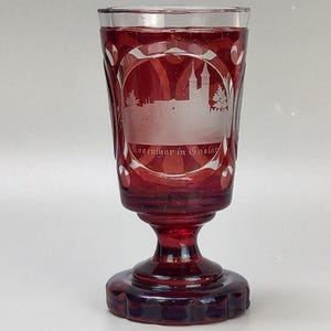 May include: A red glass goblet with a cut glass design. The goblet has a white etched image of a building with the text "Rosenburg in Gollar".