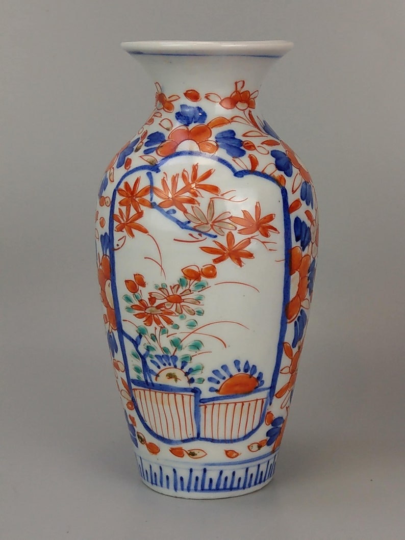 May include: A white porcelain vase with a narrow neck and a rounded body. The vase is decorated with a floral pattern in shades of blue, red, and orange.