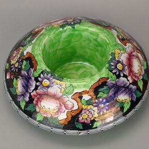 May include: A green and white ceramic bowl with a floral design. The bowl has a wide rim and a deep centre. The flowers are painted in shades of pink, purple, and yellow.
