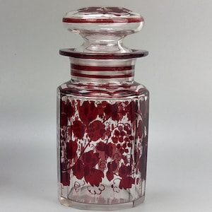 May include: A clear glass bottle with a red and white striped lid and a red grapevine design.