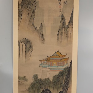 以下が含まれることがあります： 黄色い屋根の伝統的なアジアの塔が特徴の垂直風景画。霧のかかった山々と滝を背景にしています。このアートワークには漢字が含まれており、落ち着いたアースカラーで描かれています。