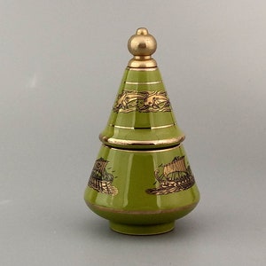 Può includere: Un vaso di ceramica verde con un coperchio dorato e bordi dorati. Il vaso è decorato con un disegno nero e oro di navi e creature marine.