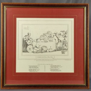 May include: A black and white satirical print titled "Comforts of Bath." The print depicts a group of people gathered around a table, with one person in the center being served food. The print is framed in a red mat and a wooden frame.