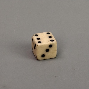 May include: A white bone dice with black dots on each side. The dice is showing the number five.