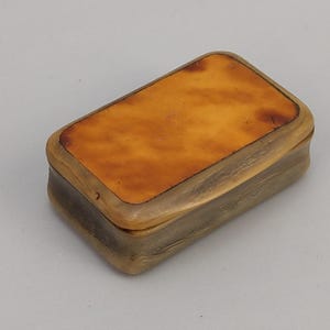 May include: A rectangular box with a light brown lid and a darker brown base. The lid has a mottled appearance, and the box appears to be made of a natural material. The box is closed and has rounded edges.
