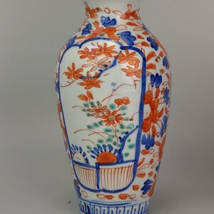 May include: A white porcelain vase with a floral design in blue, orange, and green. The vase has a narrow neck and a rounded body.