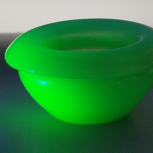 May include: A vibrant green bowl with a rounded base and a wide, circular rim. The bowl's smooth surface reflects light, highlighting its bright color. This item could be used for serving or as a decorative piece.