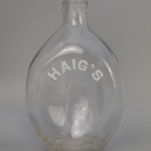 May include: A clear glass bottle with a rounded body and a narrow neck. The word "HAIG'S" is printed in white across the front. The bottle is empty and likely vintage.