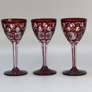 May include: Three red wine glasses with etched white designs. The glasses have a clear stem and a round bowl.