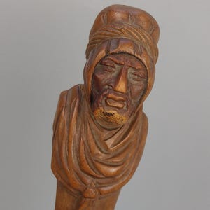 Könnte beinhalten: Eine Holzschnitzerei eines Menschenkopfes und -schulter, der einen Turban trägt. Die Schnitzerei ist detailliert und zeigt das Gesicht, den Bart und die Kleidung der Person.