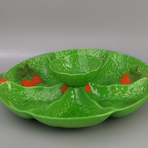 Puede incluir: Fuente de cerámica verde con diseño de hoja. El plato tiene múltiples compartimentos, incluyendo un cuenco central y varias secciones circundantes. Acentos rojos que se asemejan a tomates se colocan alrededor de los bordes.