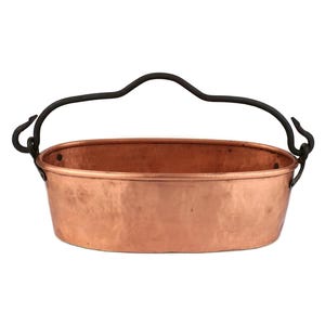 Puede incluir: Una olla ovalada de cobre con un asa de metal negro. La olla tiene un acabado martillado.