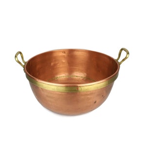 May include: A copper pot with brass handles and a brass band around the rim. The pot is empty and has a shiny finish.