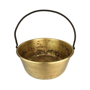 May include: A brass pot with a black metal handle. The pot has a worn, aged look.