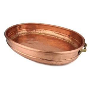 May include: An oval copper serving tray with two brass handles. The tray has a hammered finish and a slightly raised rim.