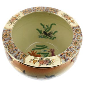 Könnte beinhalten: Eine runde, dekorative Keramikschale mit einer weiten Öffnung. Die Schale hat einen cremefarbenen Rand mit einem floralen und geometrischen Muster. Die Außenseite geht von hellbraun zu cremefarben über. Das Innere hat bemalte Blumen- und Vogelmotive.