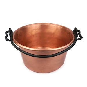 Puede incluir: Una olla de cobre con un asa de hierro negro. La olla es redonda y tiene una abertura ancha. Es una olla de estilo tradicional.