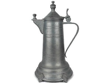Op de afbeelding: Een zilveren tinnen kan met een deksel en een handvat. De kan heeft een decoratief ontwerp op de basis.