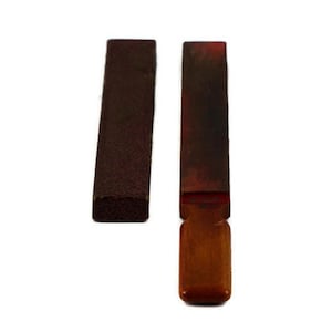 May include: Two sharpening stones, one with a wooden handle and one without. Both stones are brown and red.