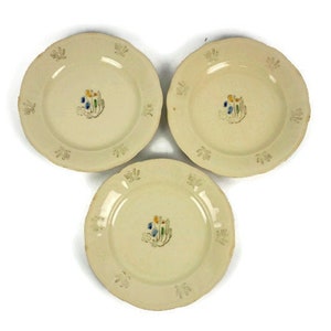May include: Three off-white ceramic plates with a raised floral design and a small painted floral motif in the center of each plate.