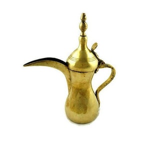 Könnte beinhalten: Eine traditionelle Kaffeekanne aus Messing mit einem Ausguss und einem Griff. Die Kanne hat einen dekorativen Deckel mit einem Knauf.