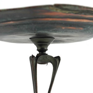 May include: A copper serving tray with a scalloped edge and a dark patina. The tray is supported by a three-legged stand with a decorative design.
