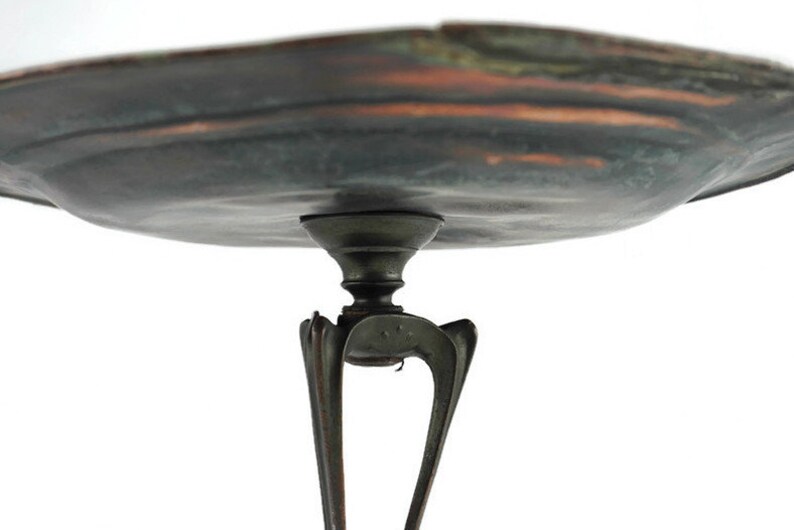 May include: A copper serving tray with a scalloped edge and a dark patina. The tray is supported by a three-legged stand with a decorative design.