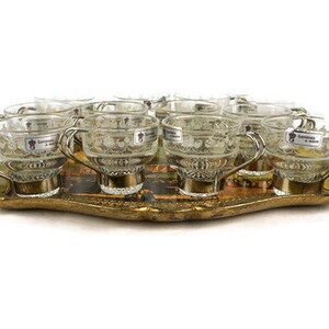 May include: A set of 10 clear glass cups with silver handles and etched designs, arranged on a gold-coloured tray with a floral pattern.