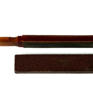 May include: A wooden and leather razor strop with a red and brown handle. The strop is in a brown leather case with the text "J. P. ROULET" and "PARIS" embossed on the front.