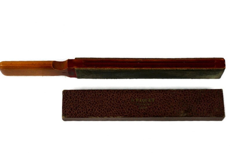 May include: A wooden and leather razor strop with a red and brown handle. The strop is in a brown leather case with the text "J. P. ROULET" and "PARIS" embossed on the front.